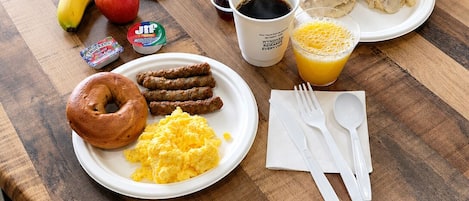 A breakfast table with waffles, sausages, scrambled eggs, a donut, a banana, an apple, a juice glass, and a coffee cup.