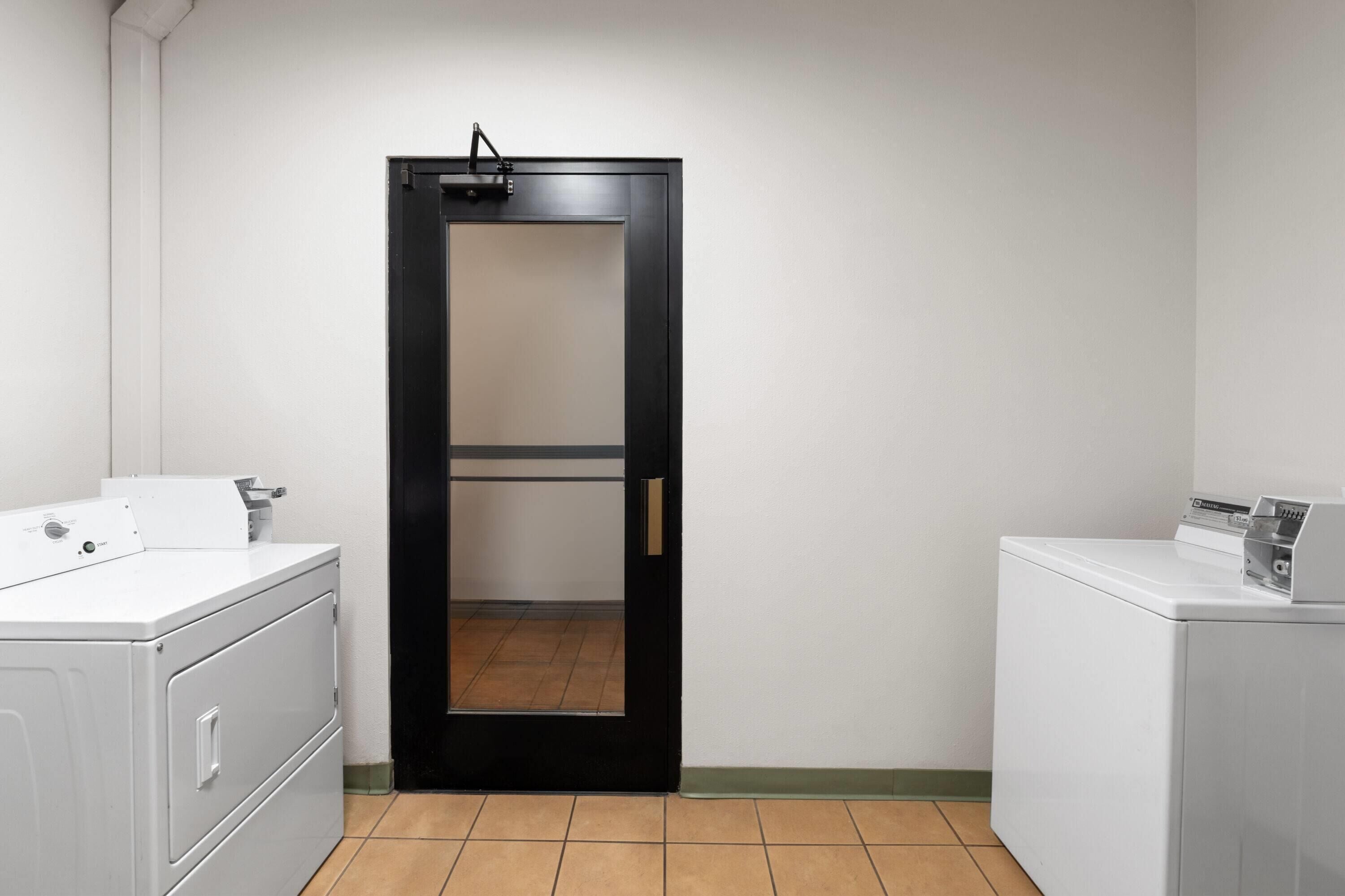 A laundry room with a black door, white washing machines, and a tiled floor.
