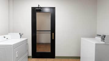 A laundry room with a black door, white washing machines, and a tiled floor.