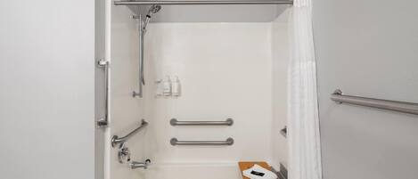 A modern bathroom with a bathtub, grab bars, a showerhead, and a wooden tray.