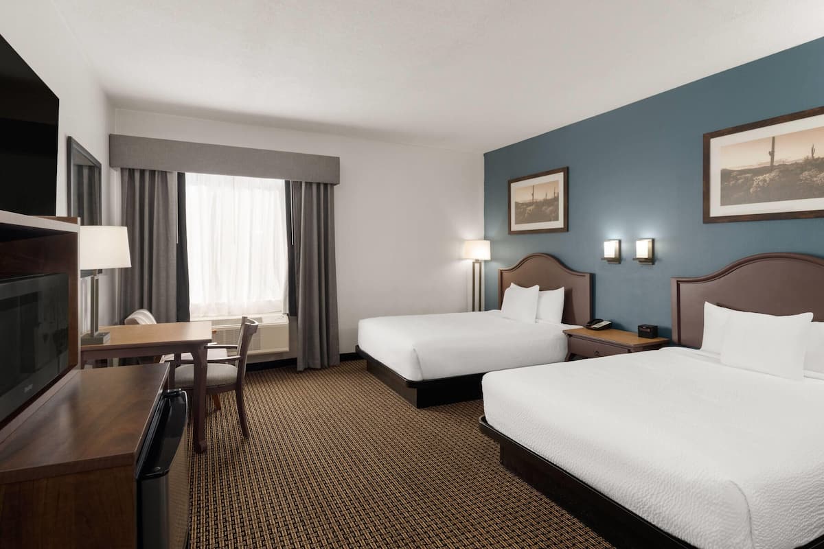 A hotel room with two beds, a desk, a TV, and a window with curtains.