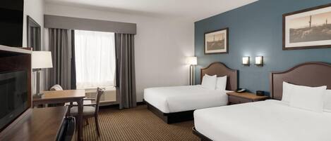 A hotel room with two beds, a desk, a TV, and a window with curtains.