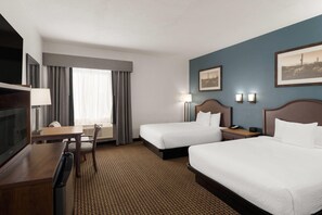 A hotel room with two beds, a desk, a TV, and a window with curtains. - Tombstone Grand Hotel, a Baymont by Wyndham (Tombstone)