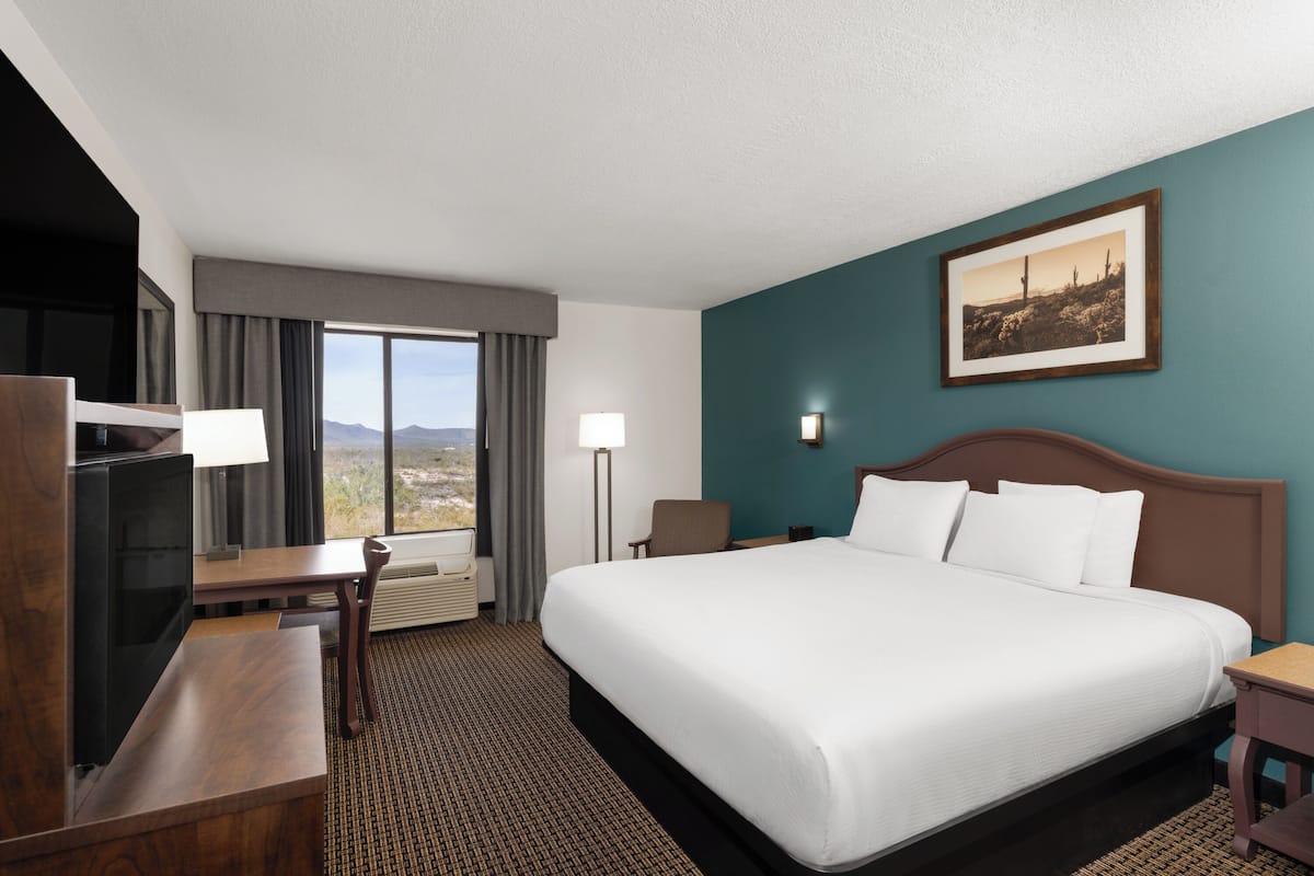 A hotel room with a bed, desk, chair, TV, and a view of the mountains.
