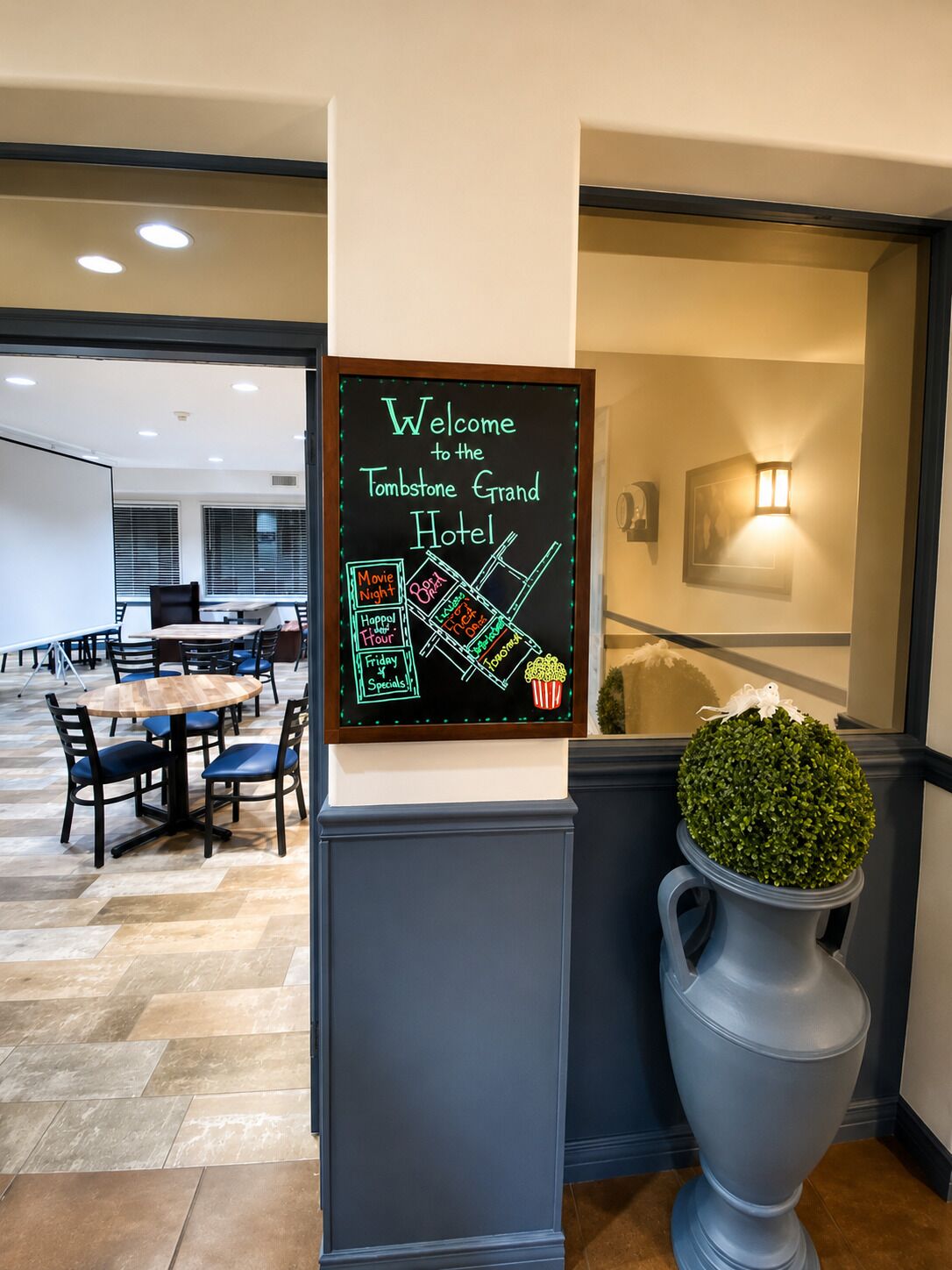 A hotel reception area with a chalkboard sign listing amenities like movie night, happy hour, and specials.