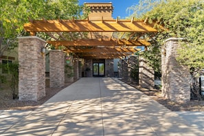 A covered walkway leading to a building entrance, flanked by stone pillars and surrounded by trees. - Tombstone Grand Hotel, a Baymont by Wyndham (Tombstone)