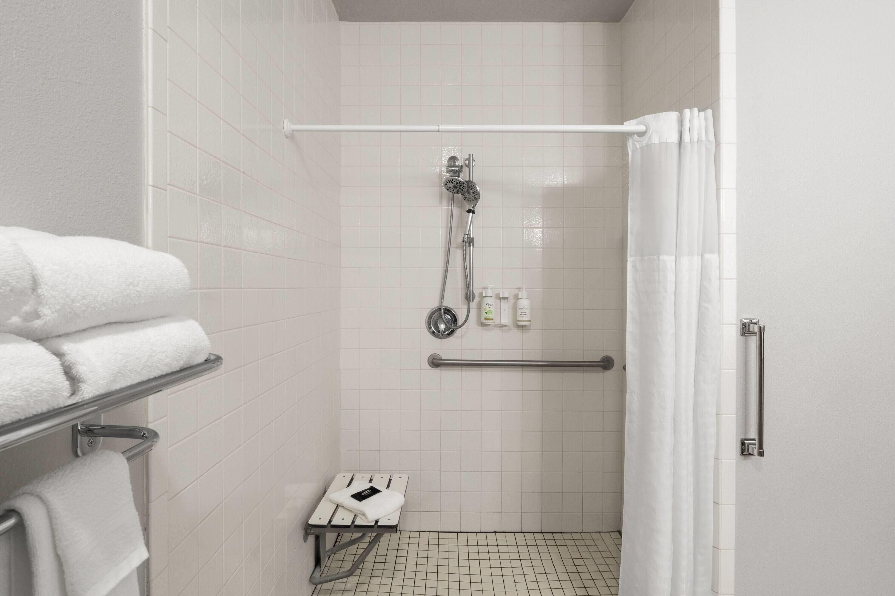 A modern bathroom with white tiles, a glass shower enclosure, a white towel rack, and a grab bar.