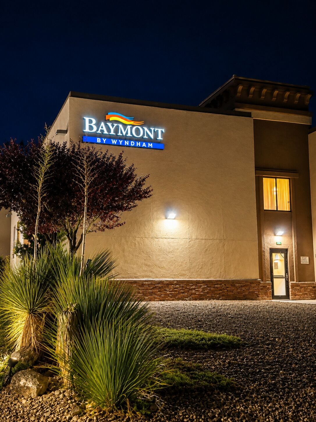 Hotel Baymont by Wyndham, con un cartel en el edificio, una entrada bien iluminada y jardines con plantas.