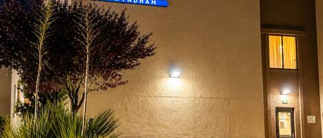 Hotel Baymont by Wyndham, con un cartel en el edificio, una entrada bien iluminada y jardines con plantas.