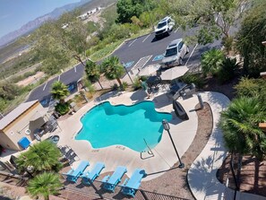 A swimming pool with blue chairs, a covered seating area, and a parking lot with a white van.