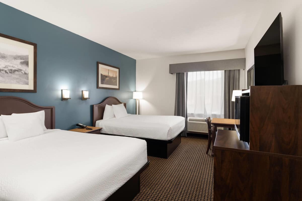 A hotel room with two beds, a desk, a chair, a TV, and a window with curtains.