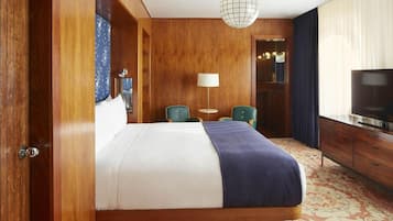 Una habitación de hotel con una cama grande, un escritorio con silla, televisor y un candelabro.