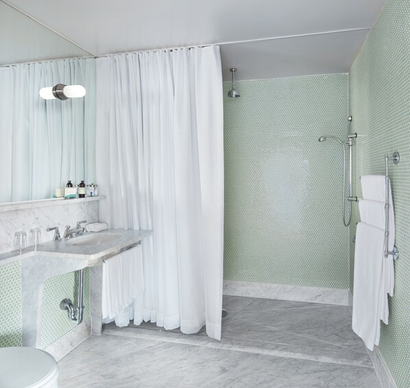 Un baño con lavabo de mármol, ducha con puerta de vidrio y retrete.