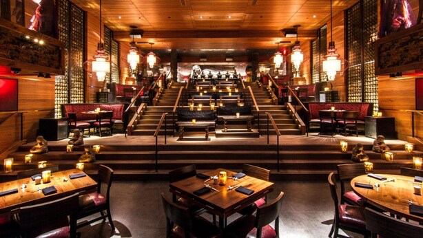 Un restaurante con un escenario central, decoración de madera y mesas iluminadas con velas.