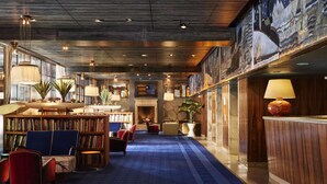 Una biblioteca amplia con estanterías, asientos cómodos y piso cubierto de alfombra azul.