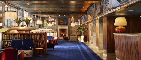 A spacious library with bookshelves, comfortable seating, and a blue carpeted floor.