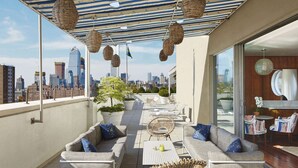 Terraza en la azotea con mobiliario de mimbre, plantas en macetas y vista panorámica de la ciudad.
