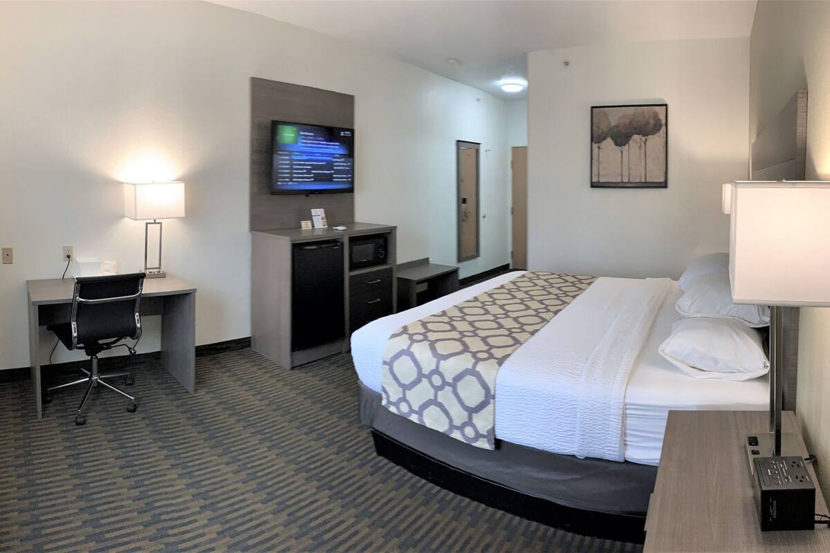 A hotel room with a bed, desk, chair, TV, and a painting on the wall.
