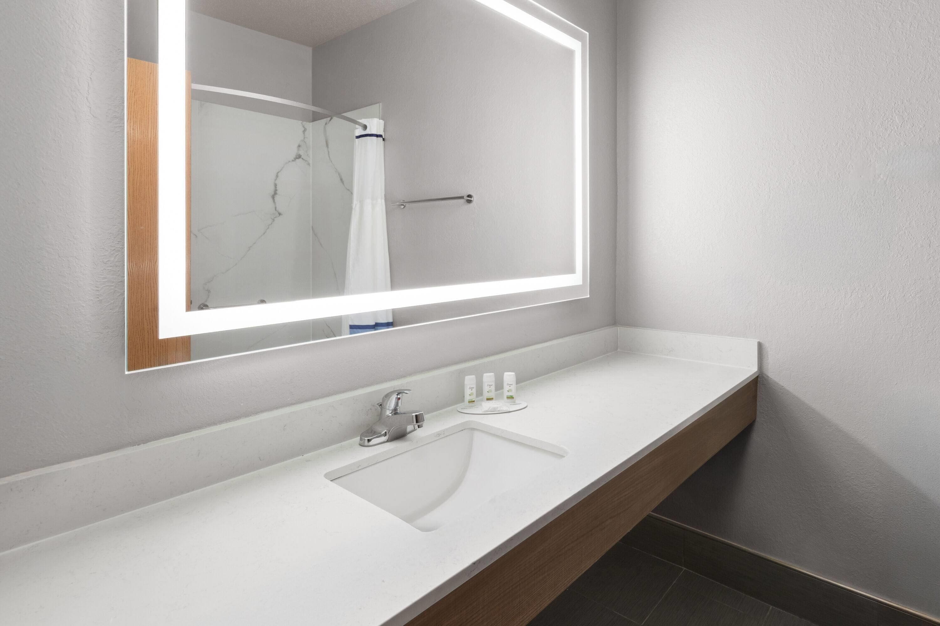 A modern bathroom with a white sink, a large mirror with LED lighting, and a wooden vanity.