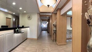 Un couloir d’hôtel avec un plancher en bois, un comptoir de réception et une horloge au mur.
