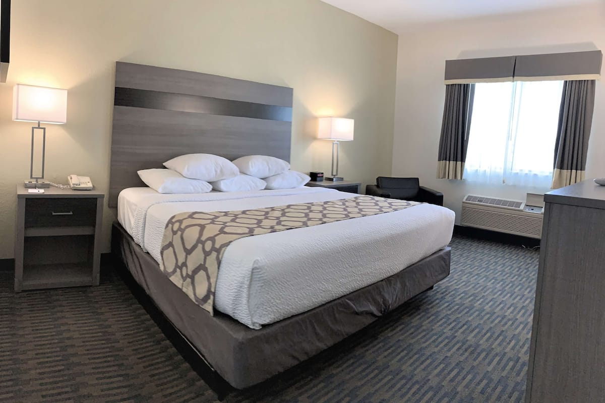 A hotel room with a large bed, two bedside tables, a desk, and a window with curtains.