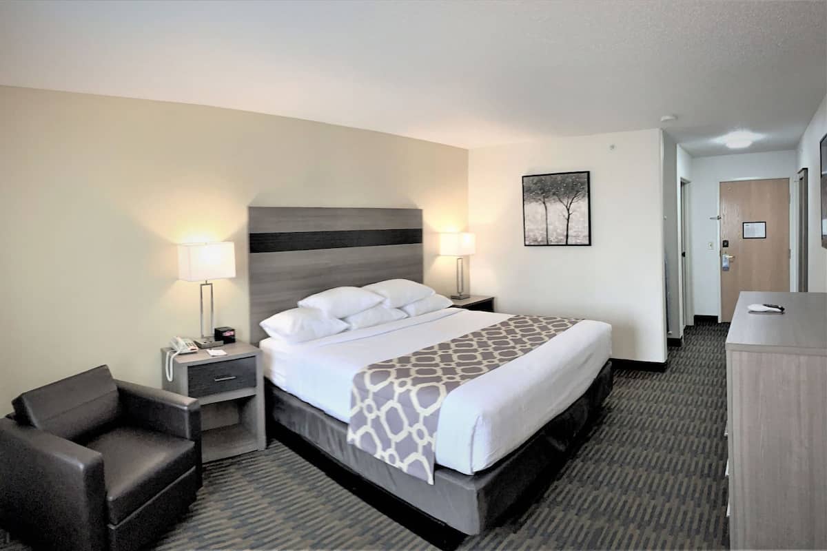 A hotel room with a bed, bedside lamps, a desk, a chair, and a framed picture on the wall.