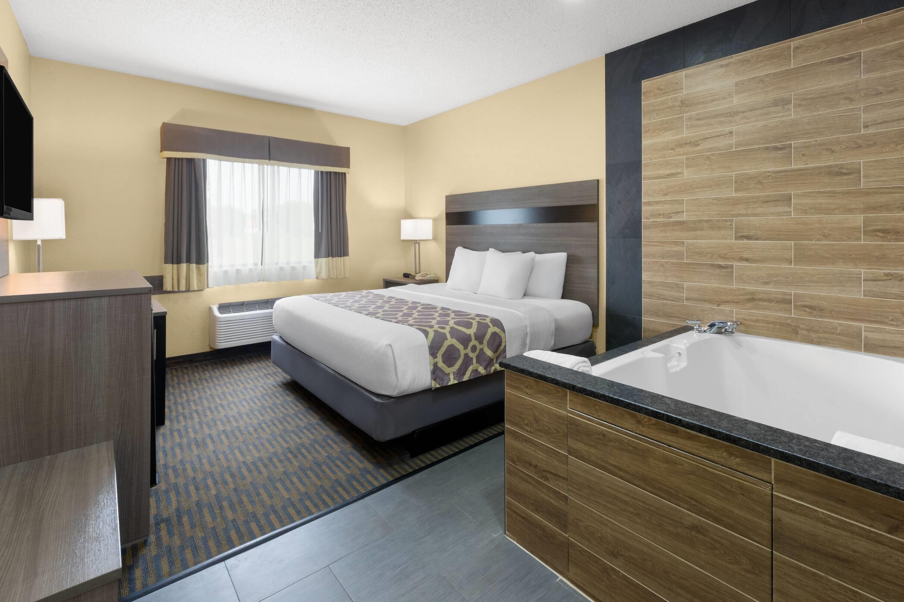 Una habitación de hotel con cama, baño con bañera, escritorio y ventana con cortinas.