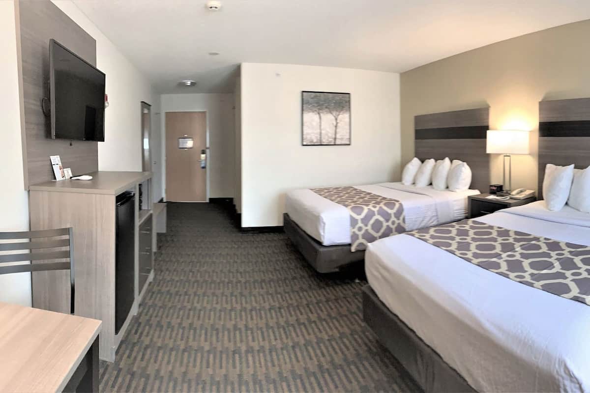 A hotel room with two beds, a desk, a chair, a TV, and a painting on the wall.
