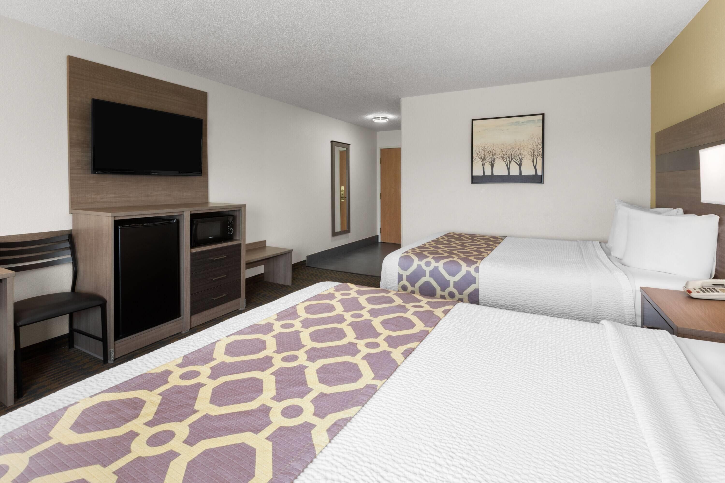 A hotel room with a TV, a desk, two beds, and a painting on the wall.