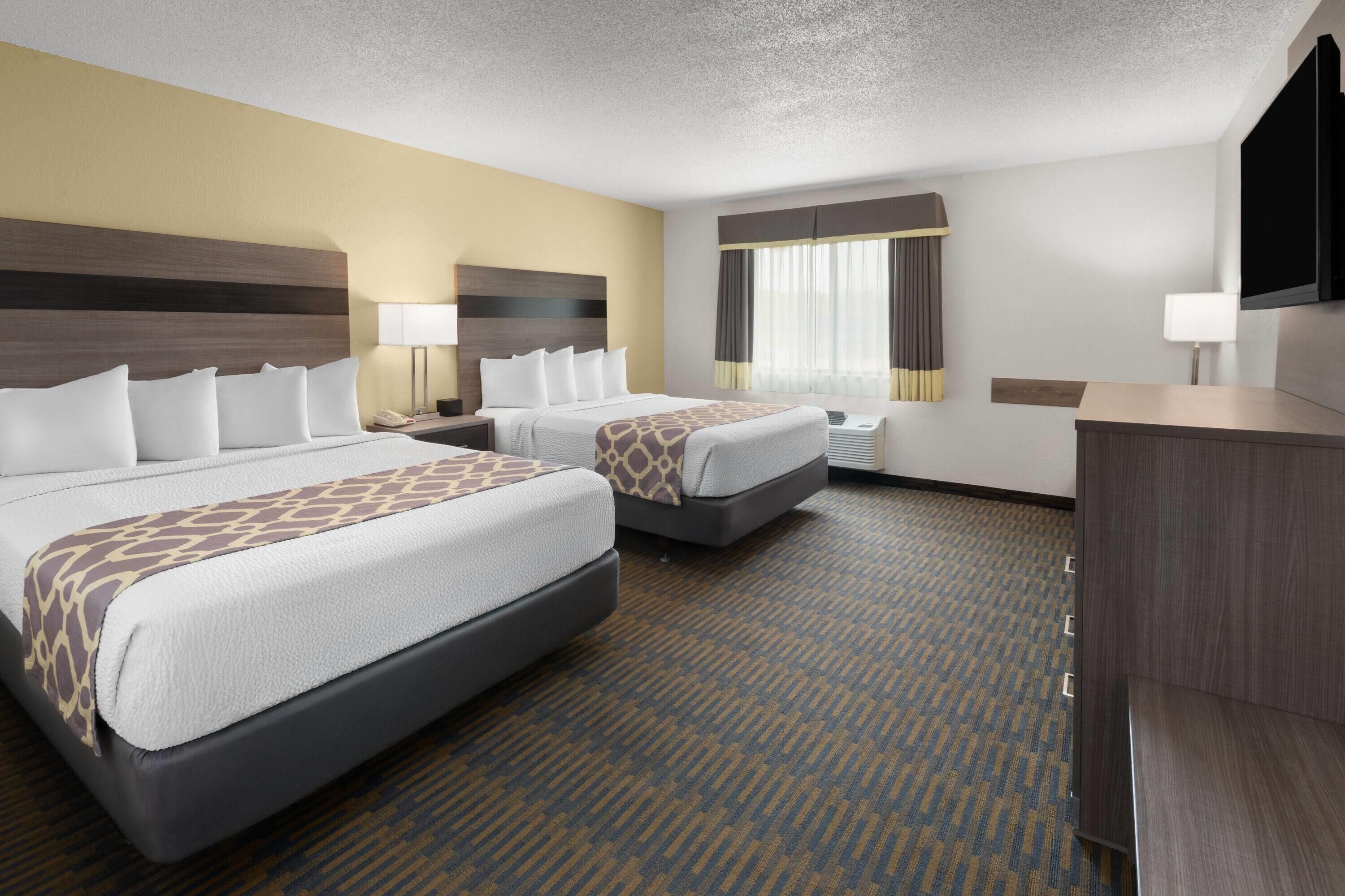 A hotel room with two beds, a desk, a TV, and a window with curtains.