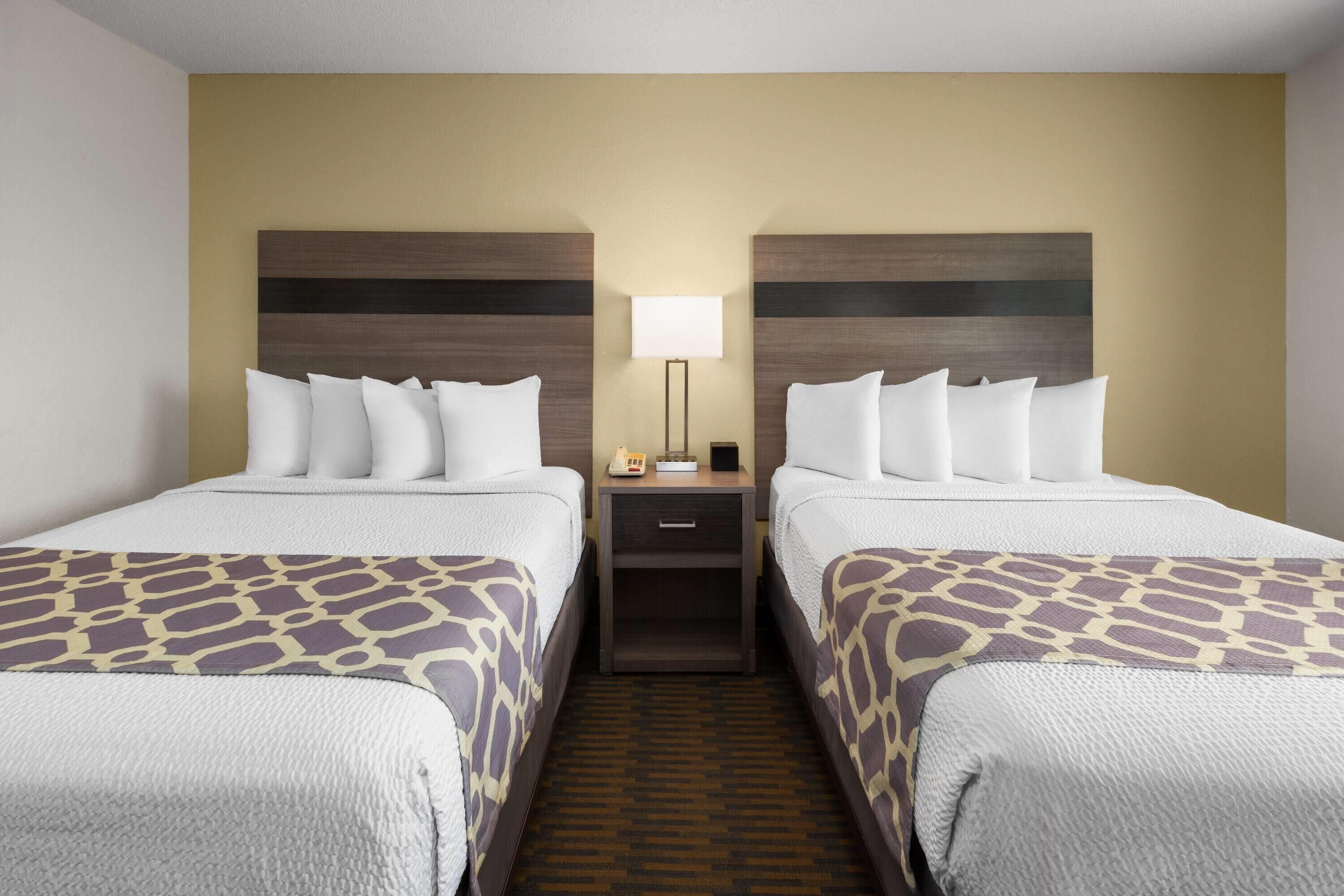 A hotel room with two beds, a nightstand with a lamp, and a patterned bedspread.