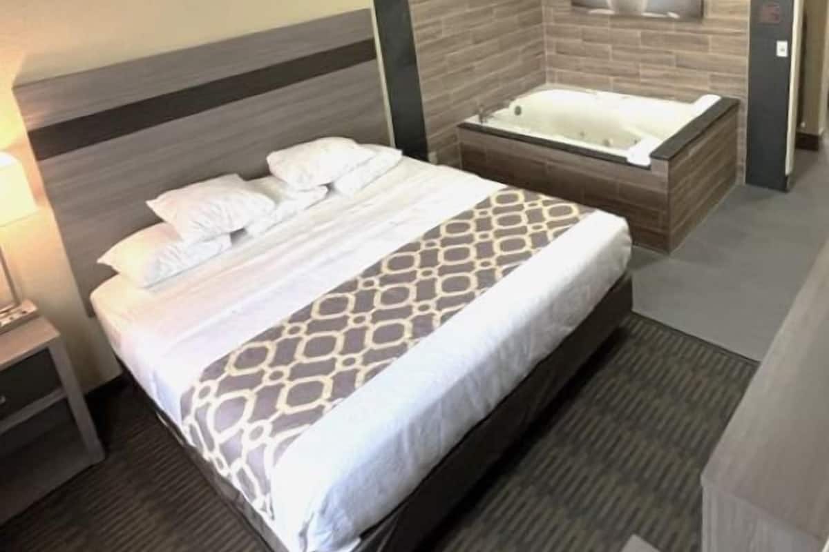 A hotel room with a large bed, a separate bathroom with a bathtub, and a wall-mounted artwork.