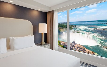 A hotel room with a large bed, a nightstand, a lamp, and a view of a waterfall.