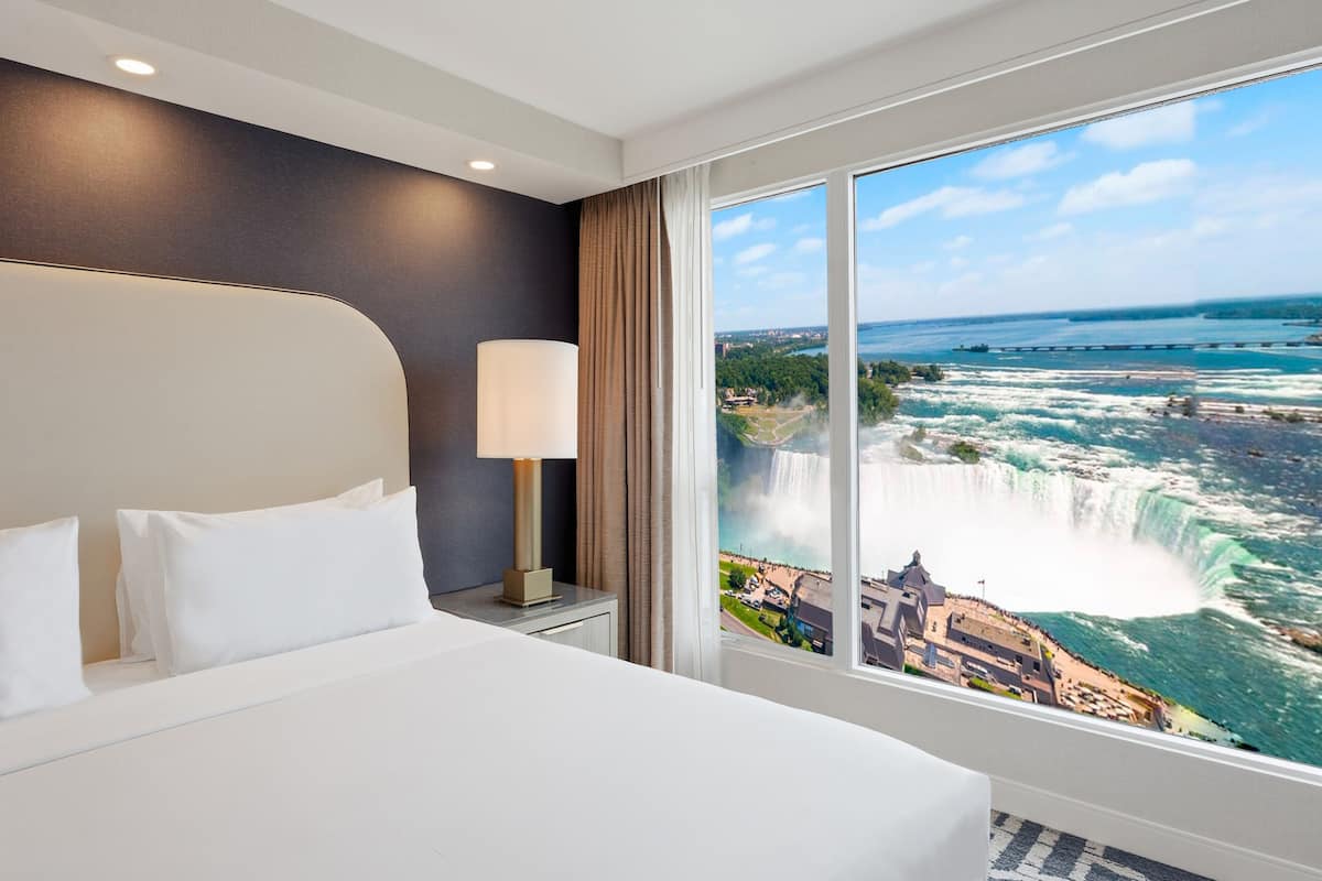 A hotel room with a large bed, a nightstand, a lamp, and a view of a waterfall.