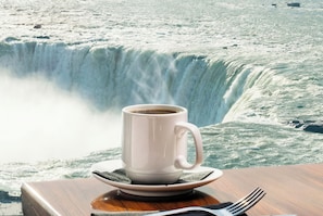 A white mug on a saucer with a fork beside it, set against a backdrop of a large waterfall. - Hyatt Regency Niagara Falls Fallsview (Niagara Falls)