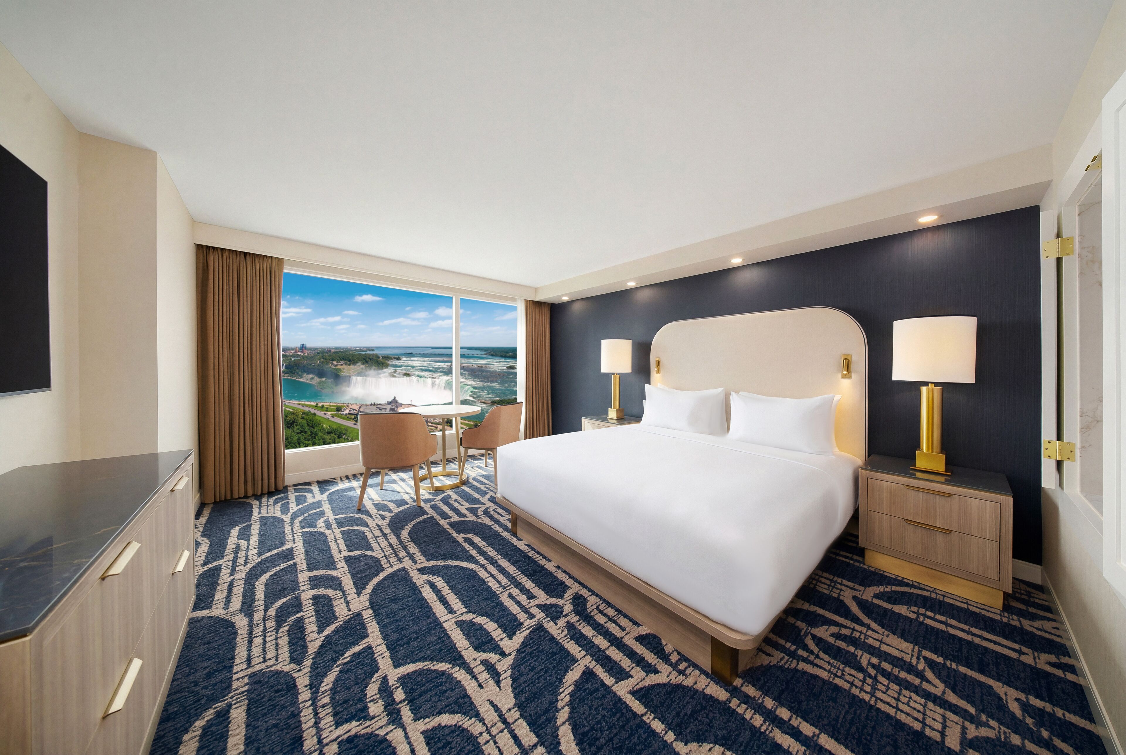Ein Hotelzimmer mit einem großen Bett, zwei Nachttischen, einem Schreibtisch und einem Sessel.