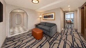 Un vestíbulo de hotel con suelo a cuadros, un sofá, una lámpara, un cuadro y una vista a través de una puerta.