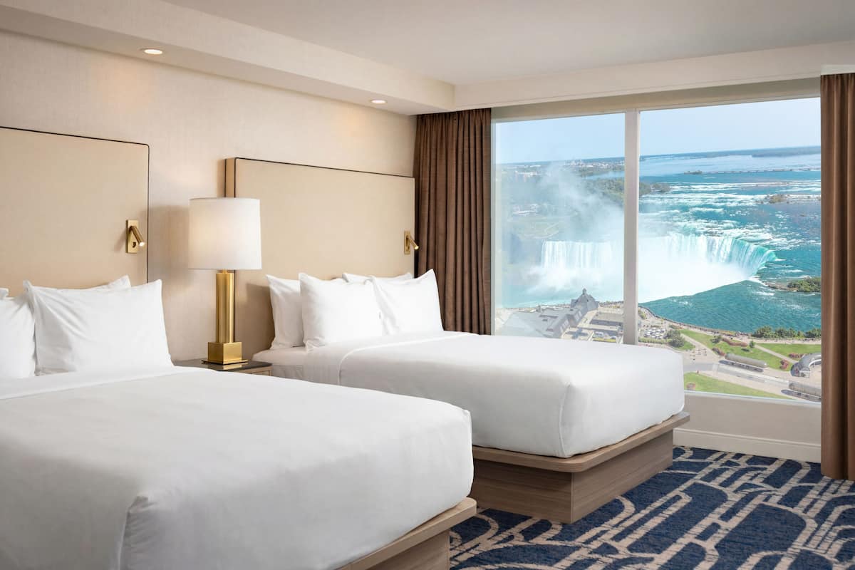 A hotel room with two beds, a large window with a view of a waterfall, and a modern lamp.