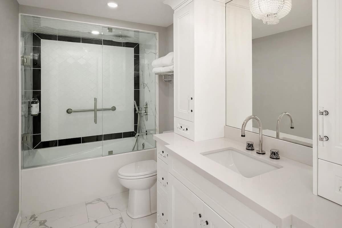 A modern bathroom with a glass shower enclosure, a toilet, a sink with a mirror, and a chandelier.
