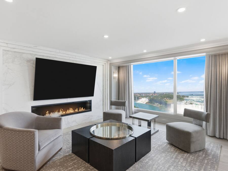 A modern living room with a fireplace, comfortable seating, a flat-screen TV, and a large window offering a scenic view.