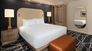Una camera d'albergo con un letto grande, due comodini con lampade, un armadio in legno, uno specchio rotondo e un tappeto decorato.
