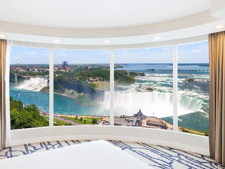A room with a large panoramic window offering a view of a waterfall and a cityscape.