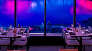 Un restaurante con mesas dispuestas para comer, amplias ventanas que ofrecen vistas a una cascada.