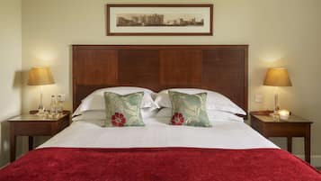 A neatly made bed with a red blanket, two bedside tables with lamps, and a framed picture on the wall.