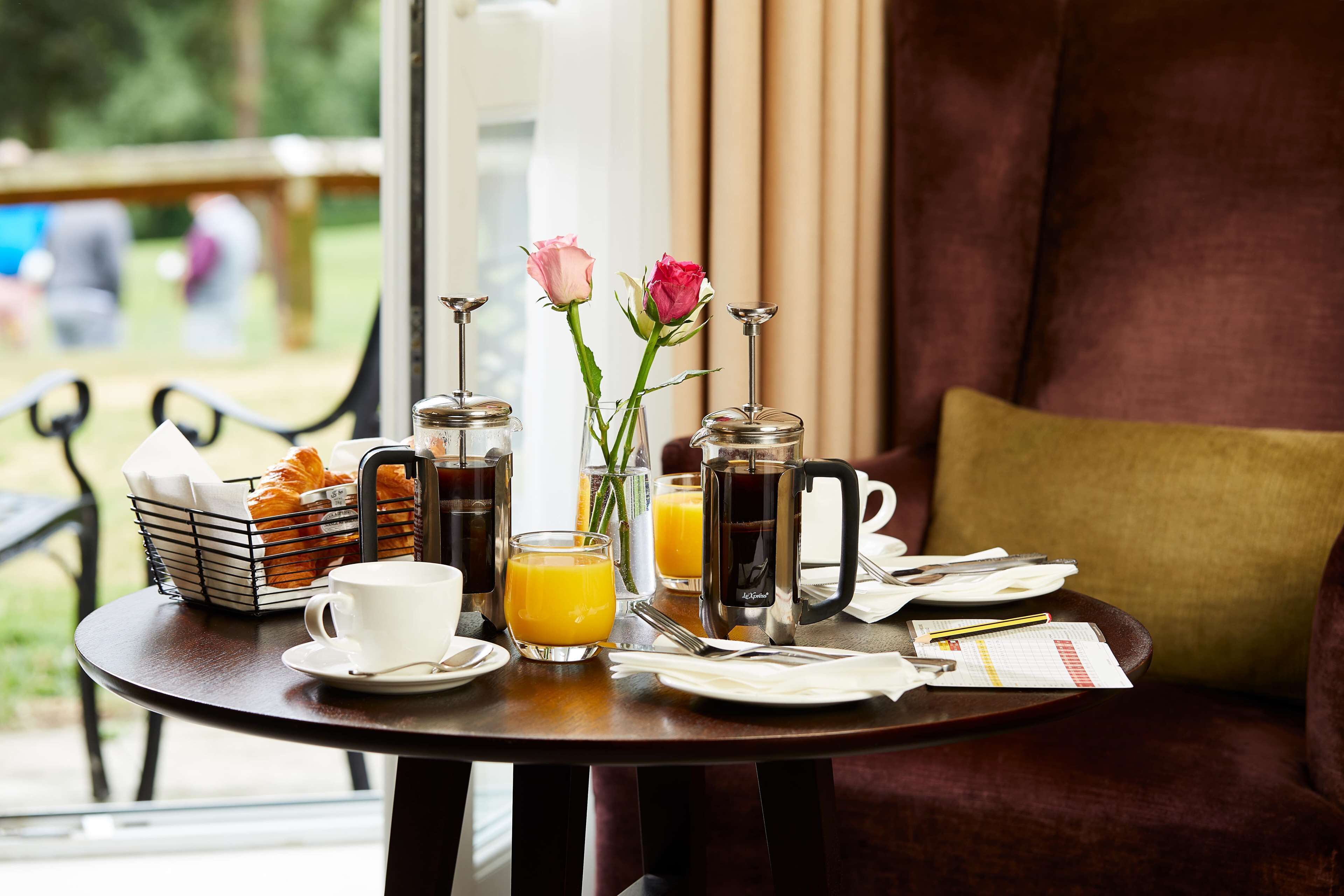 Une table de petit-déjeuner avec des croissants, du café, du jus de fruits et un vase rempli de fleurs.
