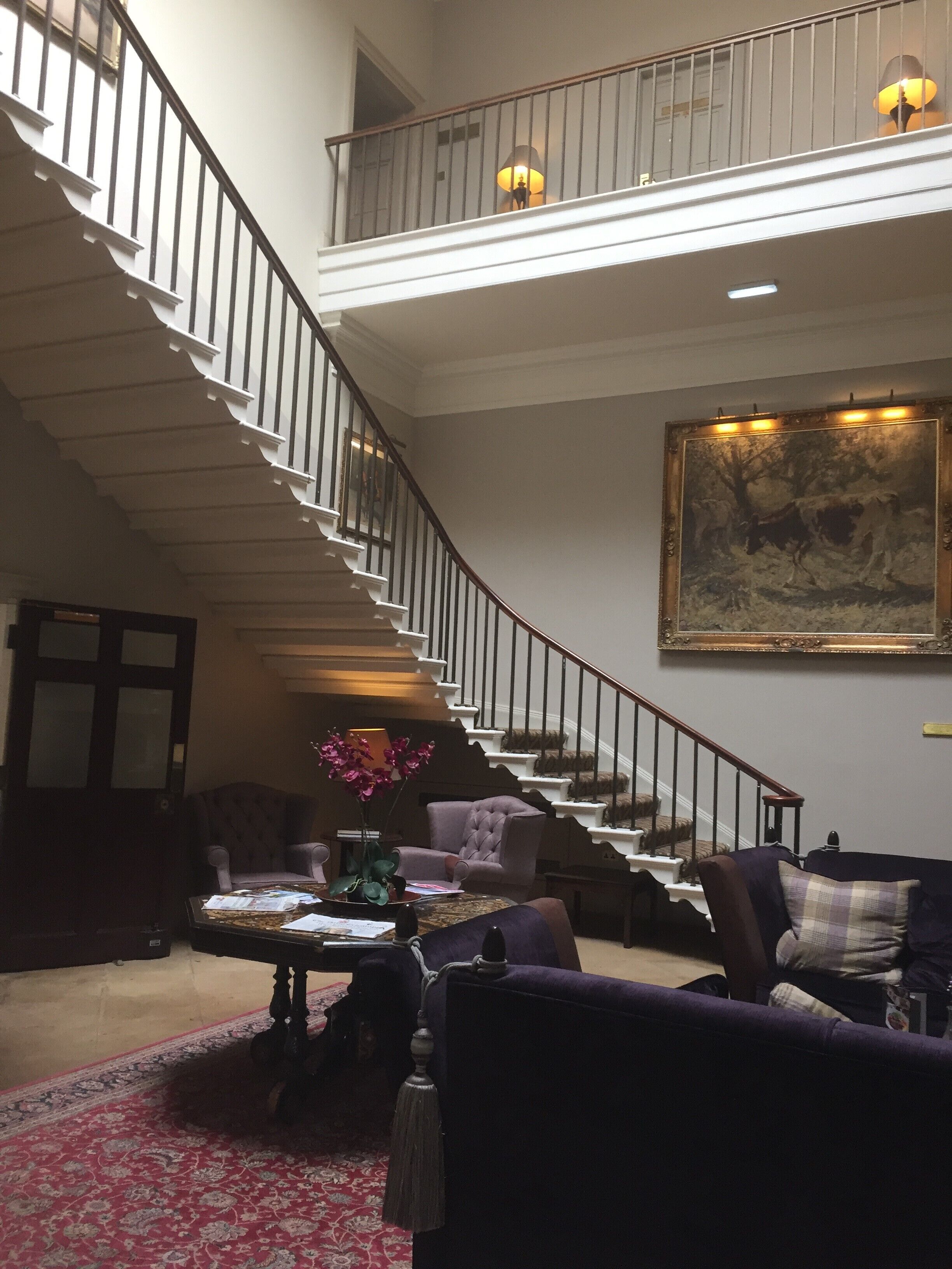 A spacious living room with a grand staircase, a large painting, and a cozy seating area.