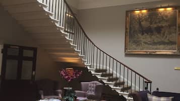 A spacious living room with a grand staircase, a large painting, and a cozy seating area.