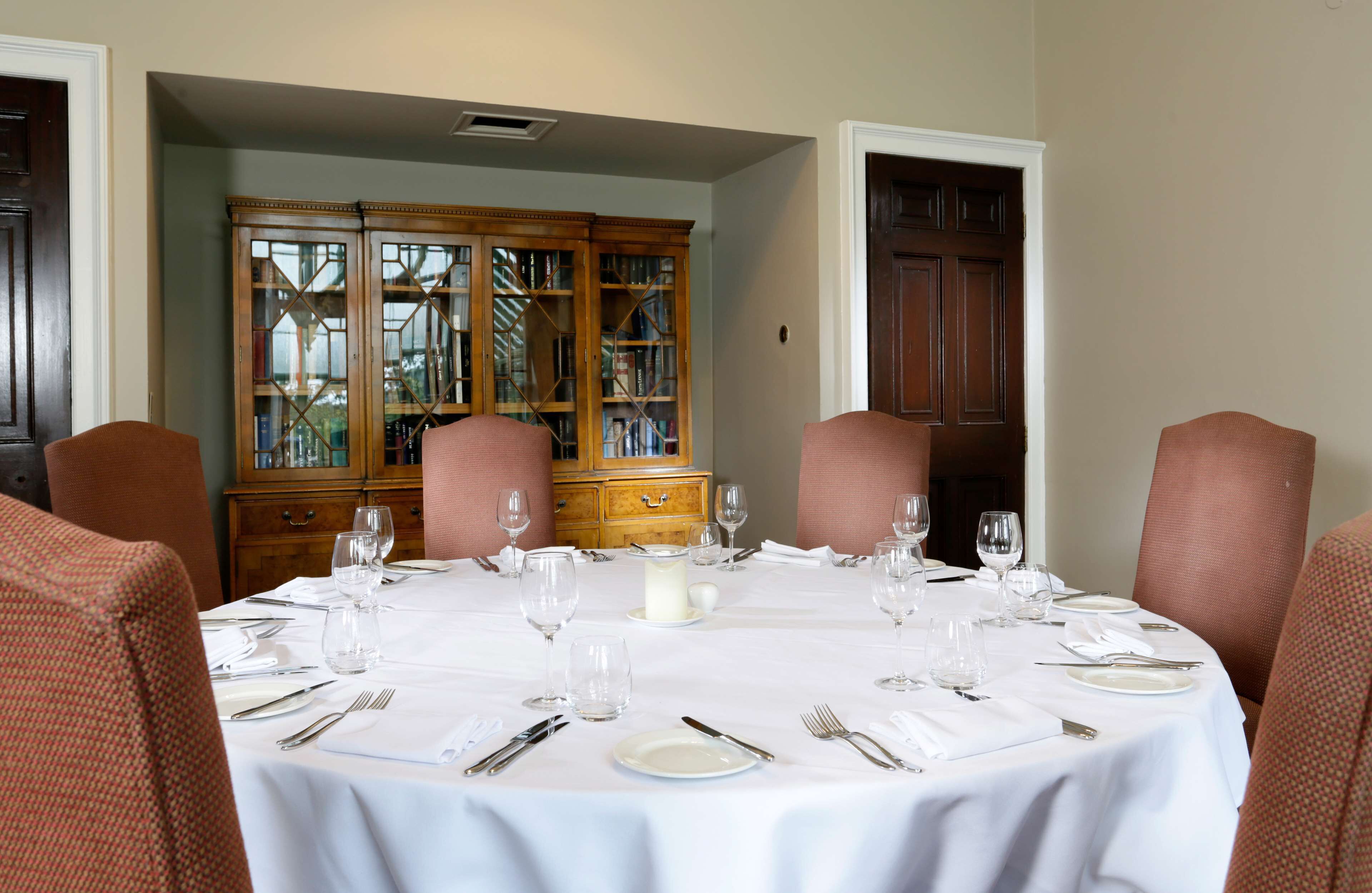 A dining room with a round table set for six, surrounded by six chairs.