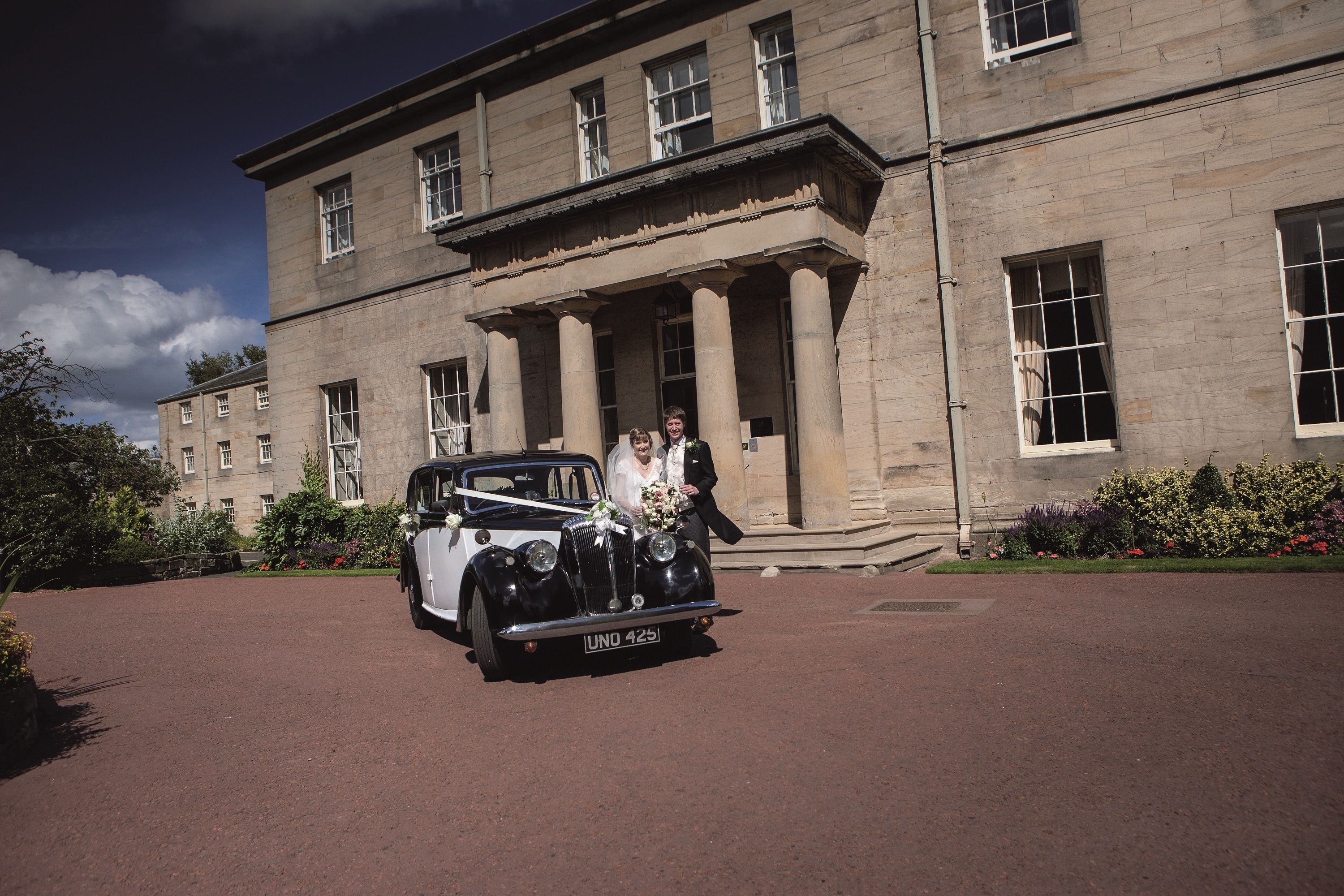 A vintage car parked in front of a large, stately building with columns and large windows.