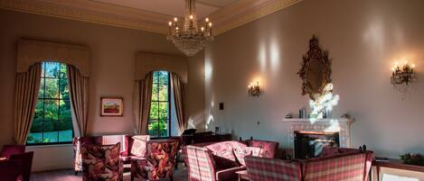 A spacious room with a fireplace, patterned carpet, and a chandelier.